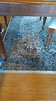 Photo showing corner of Persian style area rug under a wooden table on hardwood floor, highlighting the main body and border pattern.