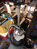 Overall view of the Sears wet dry vacuum with hose and cord, showing the cylindrical body and attachments surrounded by boxes and other items.