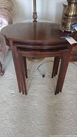 Front view of nested three piece wood table set, shows polished wood tops and tapered legs.