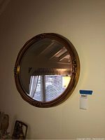 Front view of the oval wall mirror hanging on a white wall, showing its decorative gold-tone frame and reflective surface.