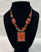 Front view of necklace on black display bust showing rectangular carnelian pendant and beaded necklace with mixed carnelian and amethyst beads.