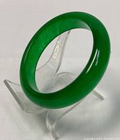 Green jade bangle on clear stand angled view, showing thickness and color depth