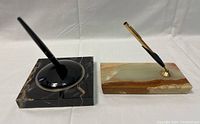 Two vintage desk pen sets, one with square black marble base and black pen, other with rectangular multicolored marble base and gold-accented pen.