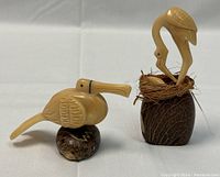 Two vintage Naya Nayon tagua bird figurines on white background, pelican on left with reattached tail, bird with nest on right
