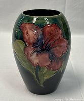 Front view of the vase showing a large red flower with green leaves against a dark green background.