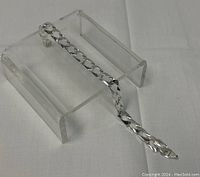 View of the full silver chainlink bracelet displayed on a clear stand, showing length and design.