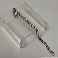 Sterling silver chain link bracelet with gold-tone diagonal stripe accents displayed on clear stand.