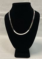 Flat herringbone silver chain necklace displayed on a black velvet bust, showing its length and pattern.