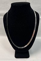 Front view of the silver necklace displayed on a black bust stand, showing the flat chain design and length.