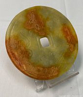 Front view of circular Chinese etched jade disc in green and brown-orange tones with a square hole in the center, displaying etched designs.
