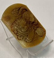 Oblique angled view of jade belt buckle showing relief carving of guardian lion motif