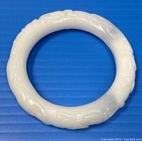 Front view of the white jade bangle showing embossed carving detail on the surface.