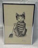 Framed black and white print depicting a cat in a striped shirt sitting in a bucket with a shovel. The print is signed bottom right by A.J. Casson.