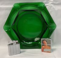 Green hexagonal blown glass ashtray with two vintage metal lighters in front, displayed on white background