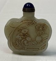 Front view showing the deeply carved bas-relief scene of two figures at a table, bottle shape and stopper.