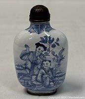 Front view of snuff bottle showing two children playing by a tree, blue enamel on white background.