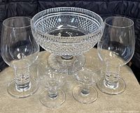 Front view of Waterford cut crystal bowl with two pairs of crystal goblets, set on a neutral surface against a dark backdrop.