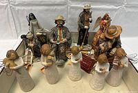 Group photo showing all 10 figurines on white fabric background. Includes the tallest praying male figurine, two seated figurines, a colorful angel, and Cheri-Lane angels with wire wings.