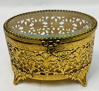 Front and side angle showing oval gold-tone filigree jewelry box with delicate openwork and four feet.