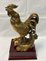 Front view of solid brass rooster sculpture on wooden base showing detailed feathers and naturalistic footing with small brass discs.