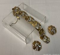 Gold-toned bracelet with clear crystals paired with two matching clip-on earrings, displayed on a stand