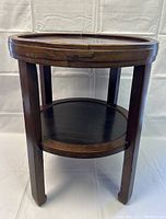 Front view of vintage round wooden side table showing four legs and lower shelf.