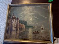 Framed oil painting on board showing coastal night scene with buildings, cliffs, moon and boats, signed K. Schatranski.