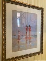 Framed artwork showing three women standing in water with reflections, in a decorative frame hung on wall.