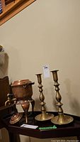 Two brass candle holders and a copper urn placed on a table against a wall.