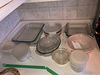 Multiple casserole dishes displayed together on countertop including glass rectangular and square dishes, ceramic dishes with floral pattern, an opaque glass lidded bowl, and plastic containers.