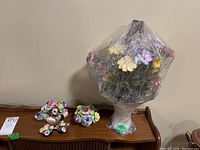Wide view of all floral arrangements and vase partially wrapped in plastic on wooden surface.