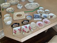 Overview of assorted bone china and porcelain items arranged on table, includes plates, bowls, ashtrays, and decorative dishes with floral and gold detailing.
