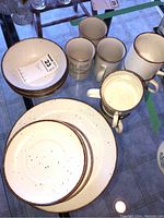 Full view of stoneware dishes including plates, bowls, and mugs with speckled cream and brown trim.