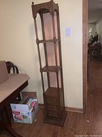 Photo of the full wooden display cabinet with three shelves and three drawers beside a wall and table.