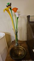 Photo of glass vase with four tall glass flowers in various colors including yellow, orange, white, and purple on a wooden surface.