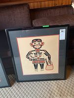 Photo of two framed prints by Henry Hunt, showing Indigenous styled figure with basket, in black and red on cream background