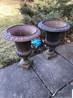 Both urns displayed side by side on concrete patio with surrounding shrubbery