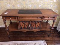 Front view of wooden sideboard with three drawers, central cabinet with metal scrollwork, slate top, placed against floral wallpapered wall.