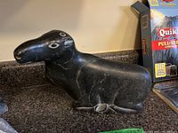 Side angled view of the black soapstone carving depicting a resting animal with white etched eyes and nostrils, showing natural white veining in the stone on a dark polished surface.
