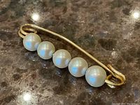 Top view of five round white pearls mounted on curved 10k gold bar pin with safety clasp.