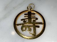 Front view of pendant showing round frame and stylized shou symbol on marble background