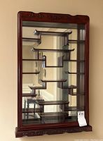 Front view of dark-stained wooden wall shelf with multiple staggered display tiers and mirrored back