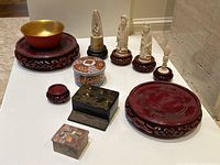 Overview of all items including four carved figures on pedestals front and center, gilt bowl, boxes, ceramic jar, and empty pedestals on white surface.