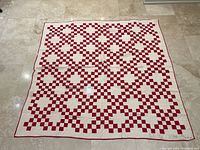 Full view of quilt laid flat on tile floor showing red and white checkerboard pattern across entire surface