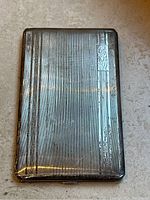Front view of sterling silver cigarette case showing worn ribbed pattern and engraved monogram plate.