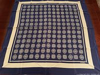 Full view of scarf laid flat showing navy background, cream border, and all-over medallion pattern with Chanel logo