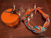 Scarf in knotted form beside the closed Hermès orange box with branded ribbon