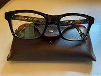 Front view of eyeglass frames resting on brown snap pouch case showing interior brand imprint and overall frame shape