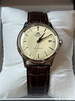 Front view of watch on cushion showing champagne dial, silver-tone markers, brown leather strap