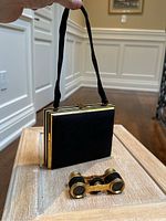 Full view of vintage black suede opera purse with gold-tone trim and attached fabric handle, shown with matching opera glasses placed in front.